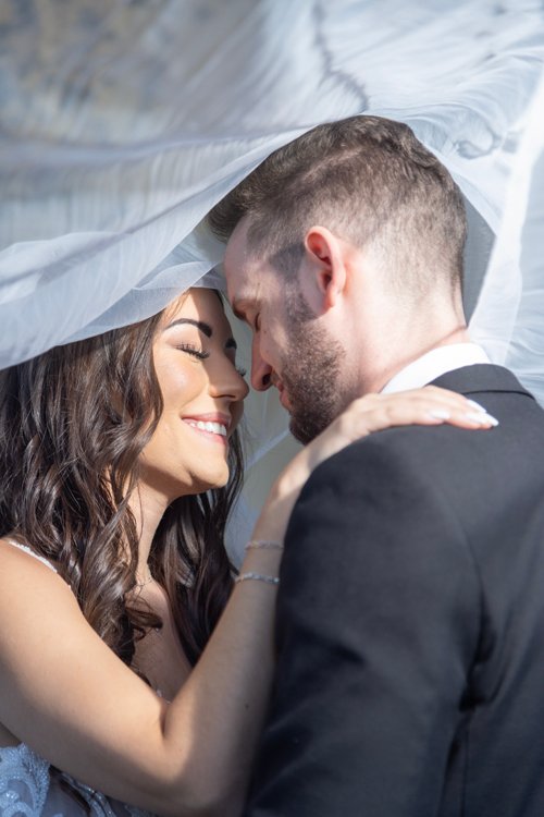 Bride and groom under white veil smiling