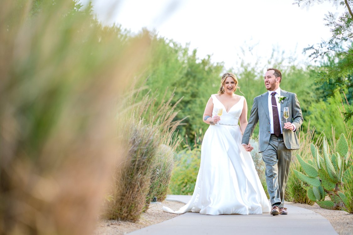 Bride and groom walking through desert landscaping at Andaz Scottsdale with artistic blurred foreground