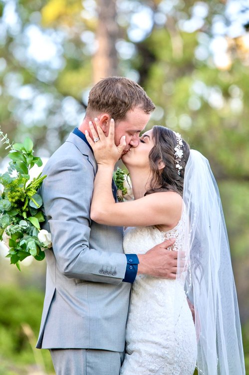 Groom embracing bride from behind in soft greenery