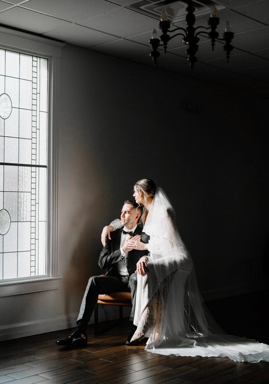 Bride and groom sitting in dramatic window-lit room