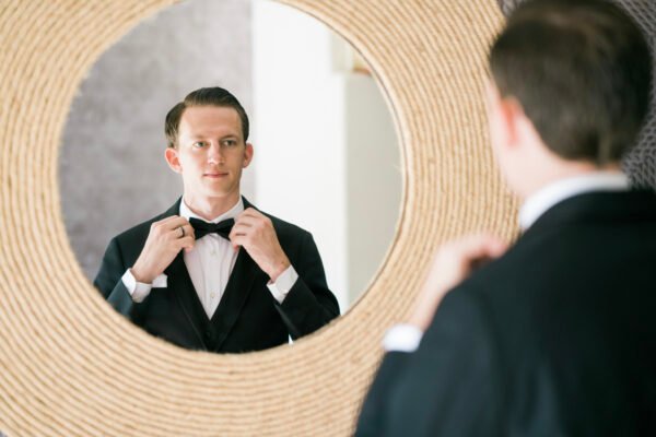 Groom adjusting bow tie in mirror