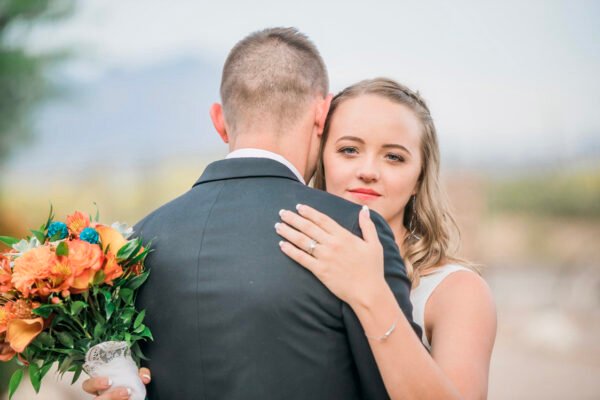 Groom hugging bride from behind in soft neutral light